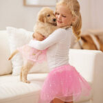 A little girl dressing her puppy in a tutu