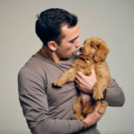 A headshot portrait of a man holding a Golden Doodle puppy dog.