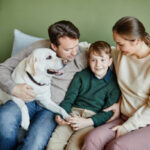 High angle portrait of happy family with dog sitting together on couch at home, copy space