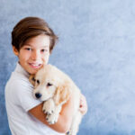 Teenage boy holding  the golden retriever baby dog by the wall